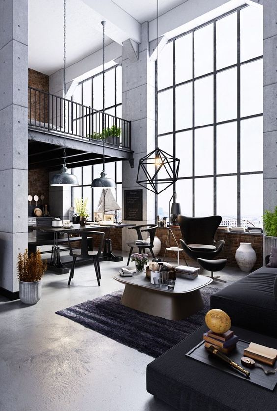 a double-height industrial living room with black seating furniture, a coffee table, a black himmeli pendant lamp and some art