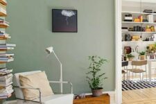 09 a Scandinavian living room with sage green walls, a neutral chair, an open shelf, a potted plant and some neutral textiles