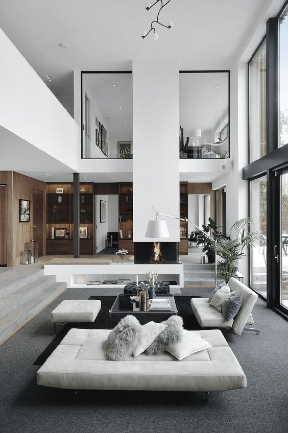 A minimalist double height living room with a glazed wall, a fireplace, grey seating furniture, a glass coffee table and a floor lamp