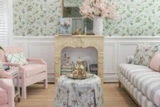 09 a pastel living room with green floral wallpaper, a striped sofa with pillows, pink chairs and a faux fireplace filled with books