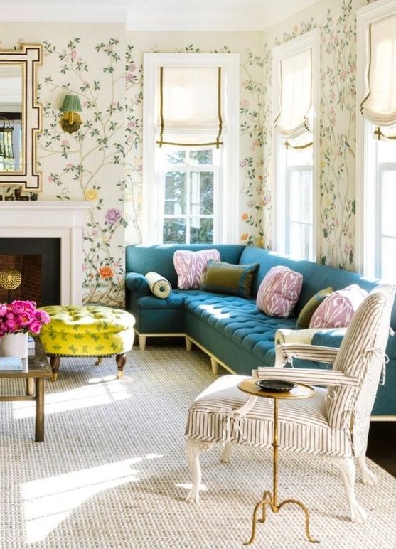 A pretty and chic living room with bright floral wallpaper, a navy sectional, a striped chair, a non working fireplace, a bold neon yellow ottoman