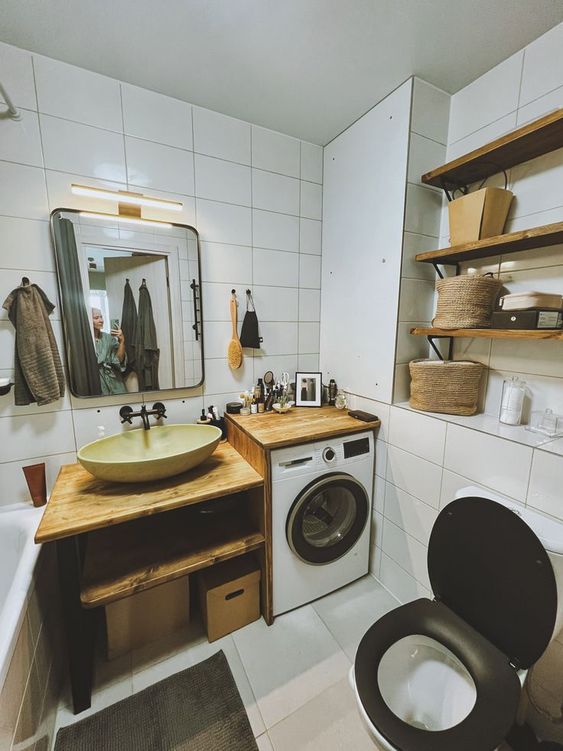 A small white bathroom clad with white tiles, with wooden shelves and an open timber vanity plus a built in washing machine