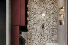 17 a bright bathroom done with terrazzo with a washing machine hidden by the shower space and behind burgundy doors