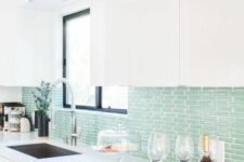 17 a modern white kitchen with sleek cabinetry, a mint green tile backsplash, black touches and white stone countertops