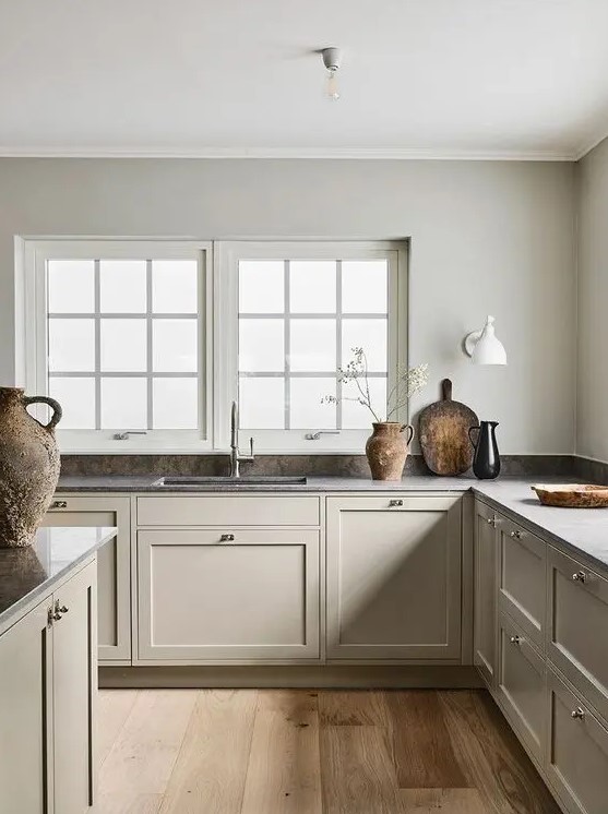 a warm and welcoming greige Scandinavian kitchen with vintage cabients and walls matching in color, dark countertops and a tiny backsplash