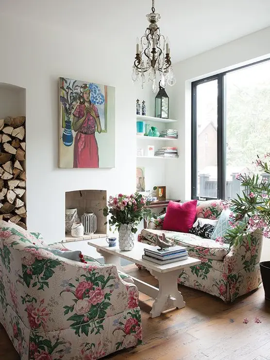 A chic living room with a non working fireplace, floral sofas, a bench as a coffee table, a crystal chandelier