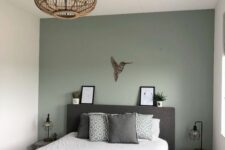 19 a small bedroom with a sage green accent wall, a dark upholstered bed, printed bedding, small nightstands and a wooden pendant lamp