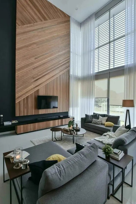 A contemporary double height living room in the shades of grey, with an accent wood slat wall, a TV and a TV unit, double height windows that bring a lot of light