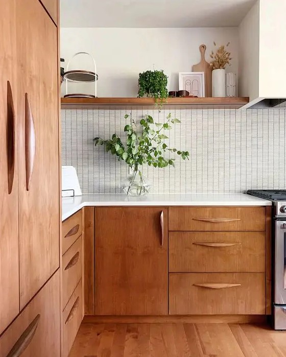 A beautiful mid century modern kitchen with stained cabinets, a white tile backsplash and white countertops, greenery for a fresh look