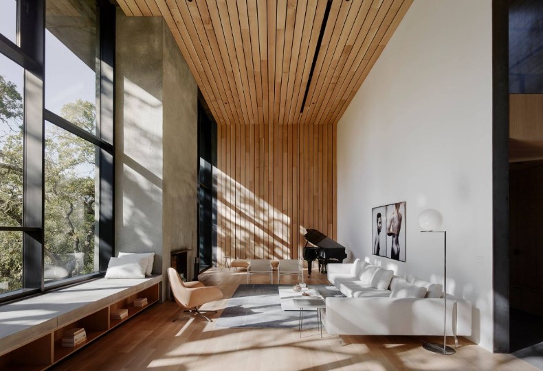 A contemporary double height living room with a large window and a windowsill bench, a white corner sofa, a coffee table and a textural slat accent wall and ceiling
