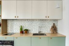 21 a two-tone kitchen with creamy and mint green cabinets, a printed tile backsplash, butcherblock countertops and built-in appliances