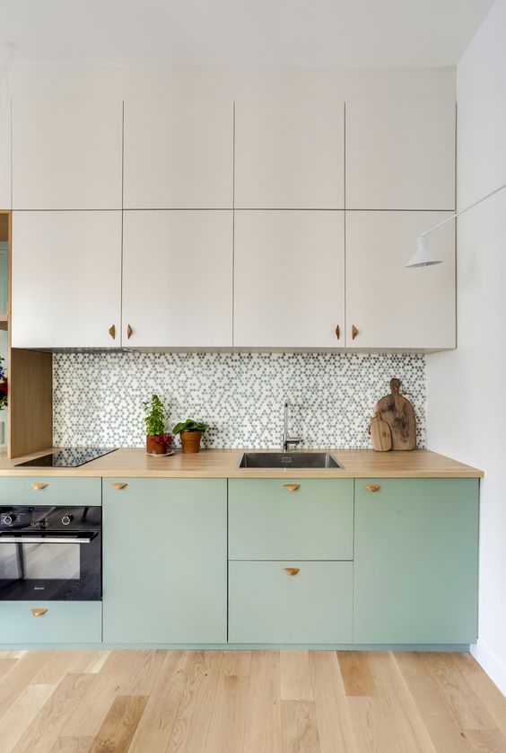A two tone kitchen with creamy and mint green cabinets, a printed tile backsplash, butcherblock countertops and built in appliances