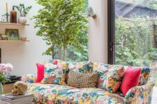 23 a neutral lviing room with glazed walls, a colorful floral sofa with bright pillows, a potted plant, a coffee table and shelves