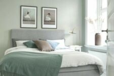 26 an airy Scandinavian bedroom with sage green walls, a grey upholstered bed with green and neutral bedding, a printed rug