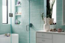 27 a beautiful mint blue bathroom clad with skinny tiles, with an oval tub, a shower space, a white floating vanity and a large mirror