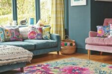 28 a bold living room with slate blue walls, a blue sofa and colroful pillows, a pink chair, a bright floral rug