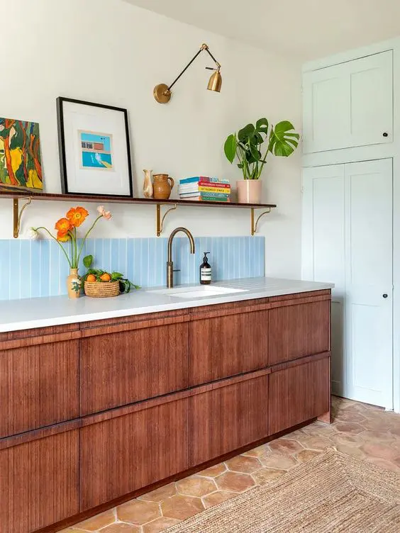 A cool and chic mid century modern kitchen with stained cabinets, white stone countertops, an open shelf, artwork and books and potted plants