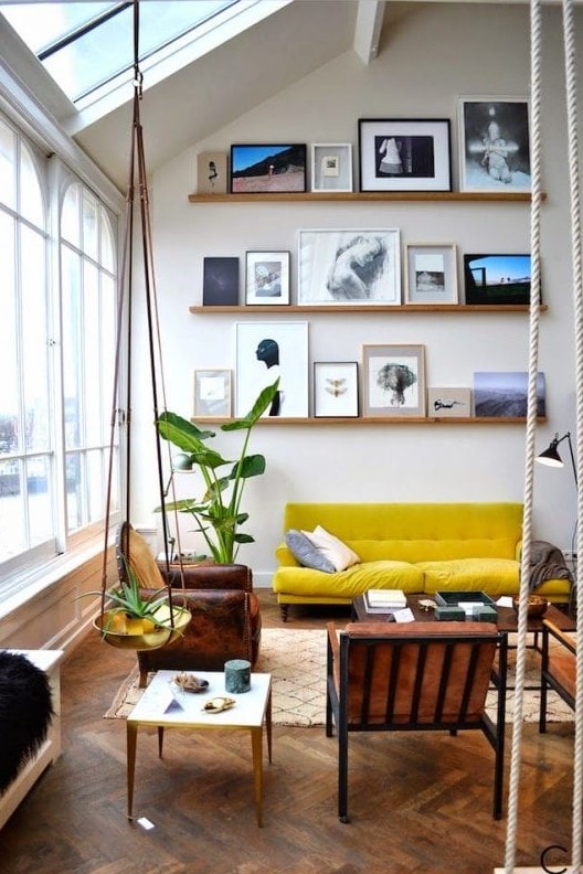 A double height living room with a ledge gallery wall, a mustard sofa, leather chairs, coffee tables and potted plants