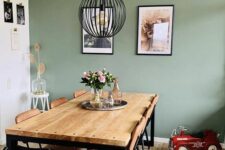 29 a modern dining room with a sage green accent wall, a stained table and leather chairs, a black pendant lamp and some art