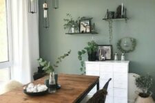 32 a Scandinavian dining room with a sage green accent wall, a rustic table, black and white chairs, pendant bulbs and open shelves