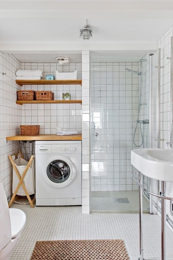 a modern white bathroom clad with square tiles, with a laundry nook with shelves and a washing machine,a  shower space and a sink