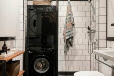 33 a Scandinavian bathroom with white square and black hex tiles, a wooden shelving unit, a shower and stacked washing machine and a dryer