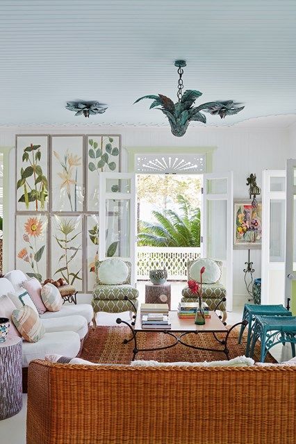 A pretty and eye catchy living room with a white sofa and a woven sofa, turquoise chairs, a coffee table, printed chairs and a floral print wall
