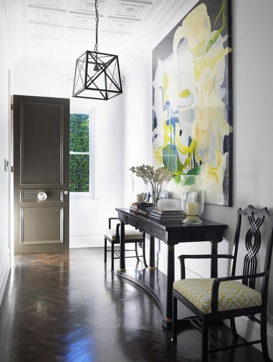 a refined entryway with dark floors, a black console and chairs, a large scale artwork that takes most of the wall