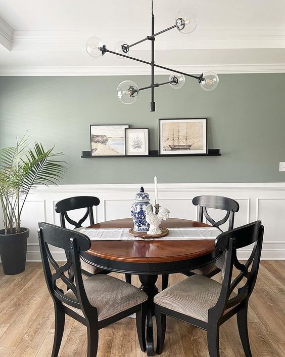 A stylish modern dining room with a sage green wall and paneling, a dark stained table and chairs, a cool chandelier and some art