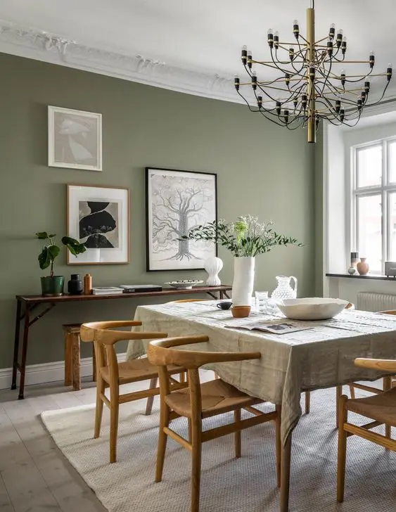 a beautiful modern dining room with a sage green accent wall, a table and wooden chairs, a console table with some decor and a gallery wall