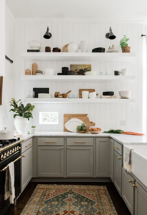 A pretty U shaped kitchen with grey shaker style cabinets, white countertops, white floating shelves and brass and gold touches for elegance