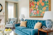 35 a vintage-inspired living room in neutrals, with a blue sofa, a colorful floral artwork, blue lamps and coffee tables