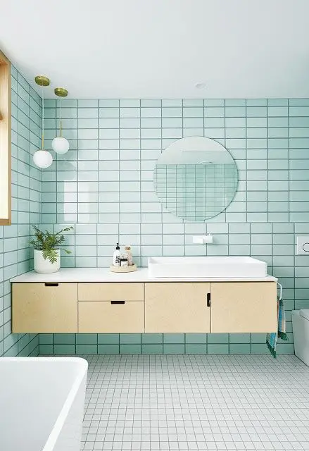 A gorgeous mid century modern bathroom clad with mint blue tiles, a plywood floating vanity, white appliances