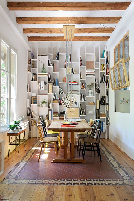 a catchy living room with a bookcase that takes a whole wall, a stained table and mismatching chairs, a small plant stand