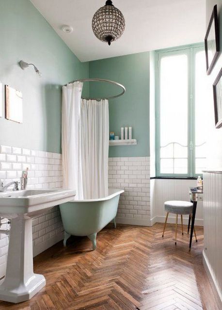 A mint blue bathroom with white subway tiles, a mint blue clawfoot tub, a free standing sink and a chic pendant lamp