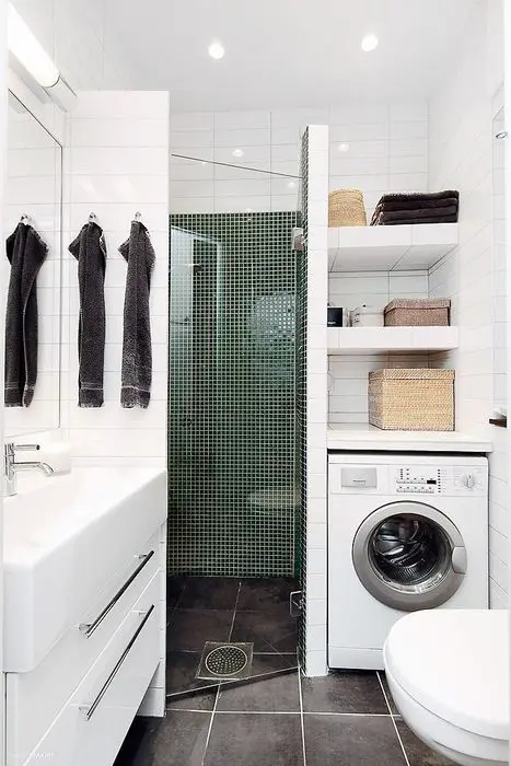 a small modern bathroom with a shower space, a white vanity, a small laundry nook with shelves and a washing machine