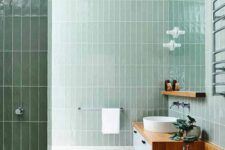 39 a stylish mint green bathroom clad with skinny tiles, with a floating wooden vanity and a round sink, a potted plant