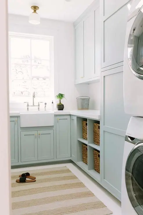 a mint blue laundry with shaker cabinets, white stone countertops, a white sink and a vintage faucet is a lovely space to do the washing