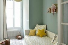 43 a chic sage green kids’ room with a storage bed and bright bedding, baskets with toys and house-shaped shelves