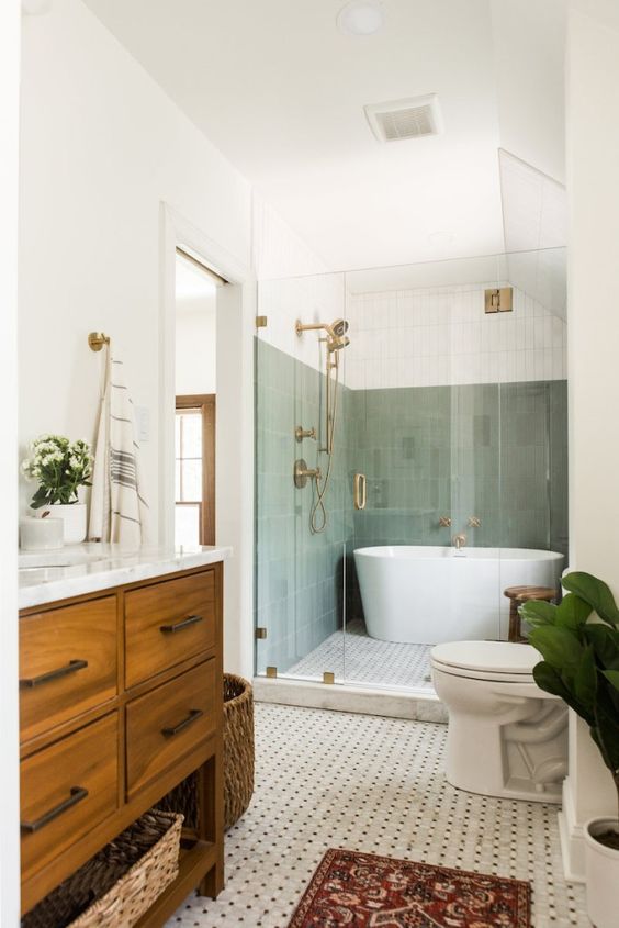 A mid century modern bathroom with sage green tiles in the bathing zone, a printed tile floor, a stained vanity and a basket