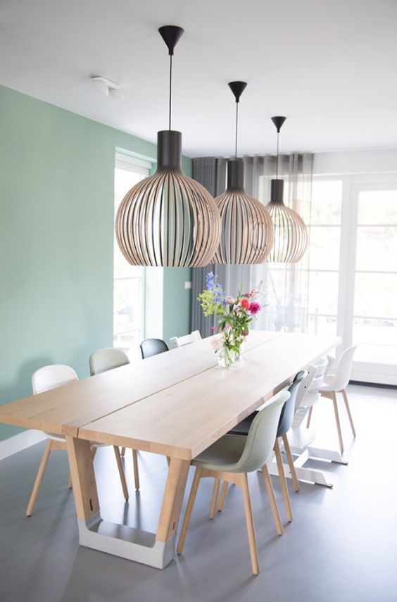 a Scandinavian dining room with a mint green accent wall, a stained table and mismatching chairs plus oversized lamps