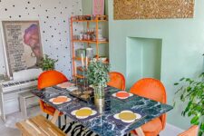 57 an eclectic boho dining room with a mint green accent wall, an orange shelving unit, orange chairs, a dark table and a bench