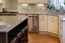 a beautiful kitchen with creamy shaker cabinets, a rich-stained kitchen cabinet and stools, a creamy tile backsplash and grey granite countertops