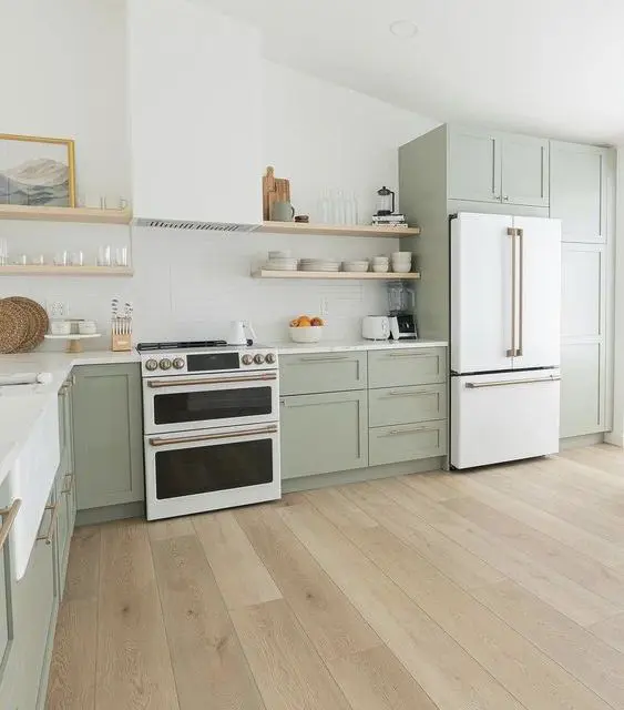 a beautiful sage green farmhouse kitchen with shaker cabinets, open shelves, a hood, a white cooker and brass fixtures