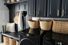 a black mudroom entry with shaker cabinets, an open storage unit with baskets, potted plants and a washing machine and a dryer