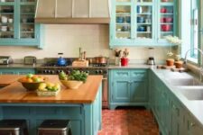 a bright blue kitchen with terracotta tile on the floor, a large vintage hood, butcher block countertops and a patterned ceiling