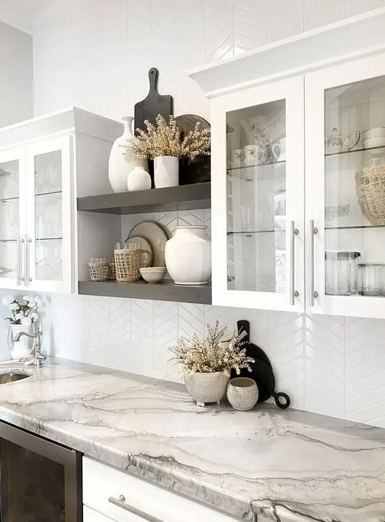 A catchy kitchen with white flat panel and glass cabinets, black built in shelves and built in appliances, a white chevron backsplash