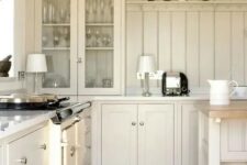 a chic cottage kitchen with tan shaker cabinets and a matching beadboard backsplash plus cool lamps is cozy and cool
