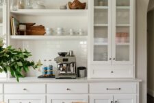 a chic white kitchen with shaker style and glass front cabinets, built-in shelves, a white tile backsplash and white marble countertops