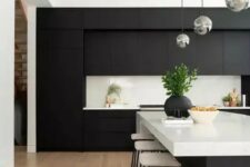 a contemporary black and white kitchen with matte cabinets, white countertops and a backsplash and bubble lamps